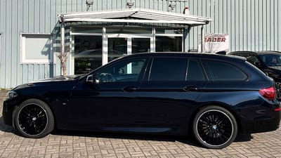Dunkelblauer BMW 5er in einer Hofeinfahrt, seitlich fotografiert, die Original-Felgen sind schwarz mit silbernem Felgenrand