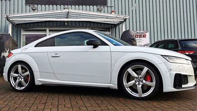 Audi TTS in Weiß vor einem Firmengebäude, seitlich aufgenommen, mit silbernen Original-Felgen im 5-Speichen-Design