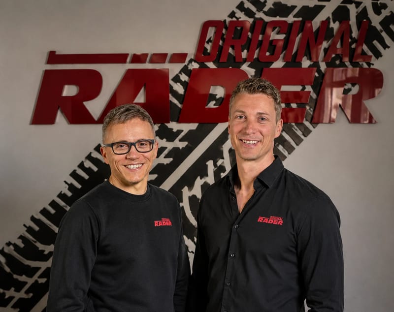 Die Geschäftsführer Tony Kasten und Christoph Wanitschke in schwarzen Firmenhemden vor der roten Original Räder Wandschrift