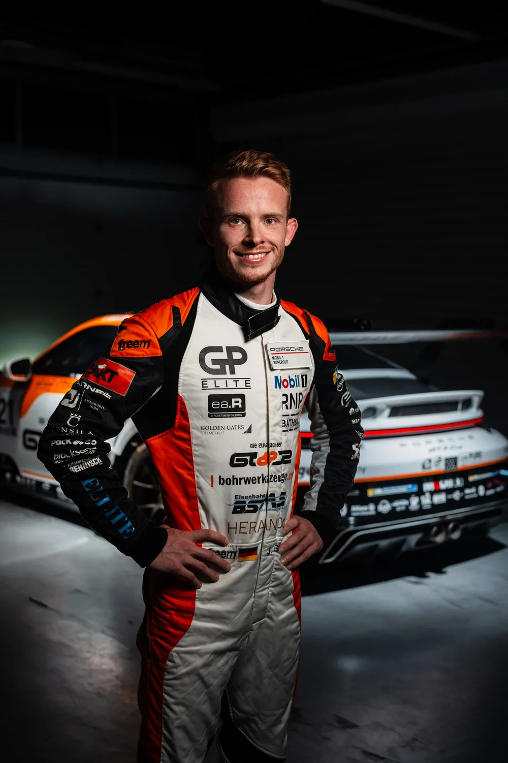 Jonas Greif w kombinezonie wyścigowym obok swojego Porsche 911 Cup